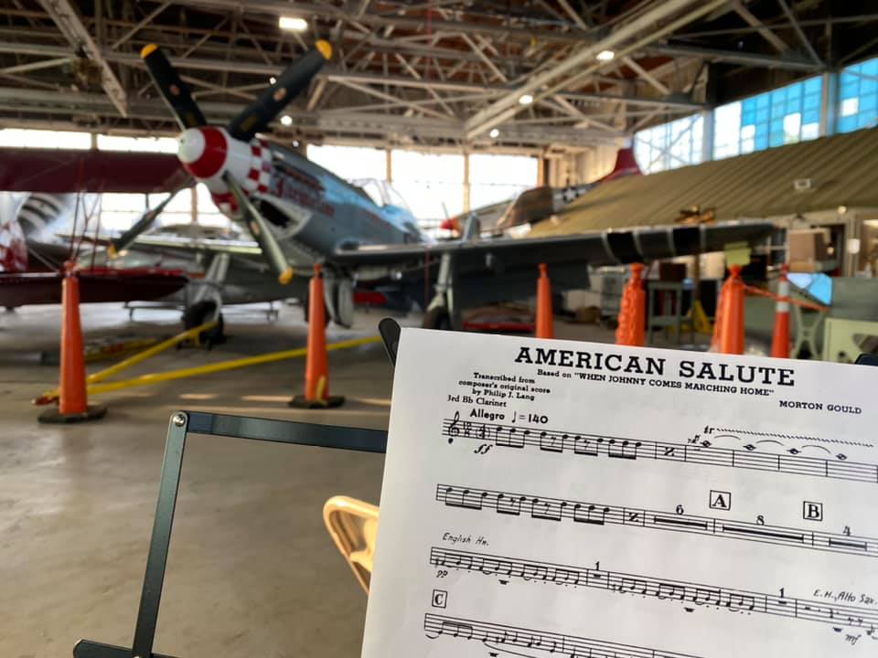 Photo of a vintage WWII plane in background with sheet music for the song American Salute in the foreground