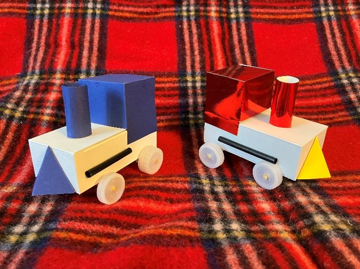 plaid background with images of two cardboard toy trains, one with blue accents and one with red and yellow accents