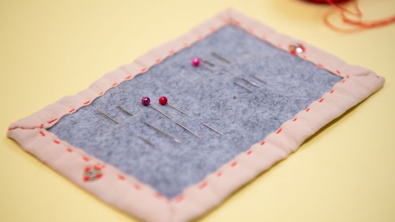 A piece of rectangular fabric handsewn around the edges with colorful pins through the it.