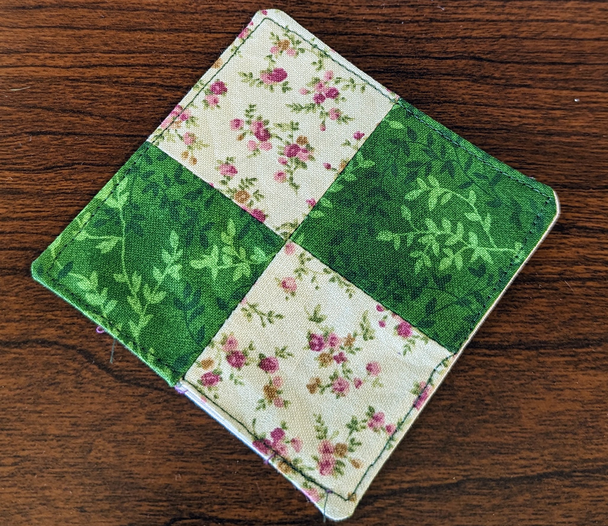 A square coaster with alternating floral patterns on a wood table.