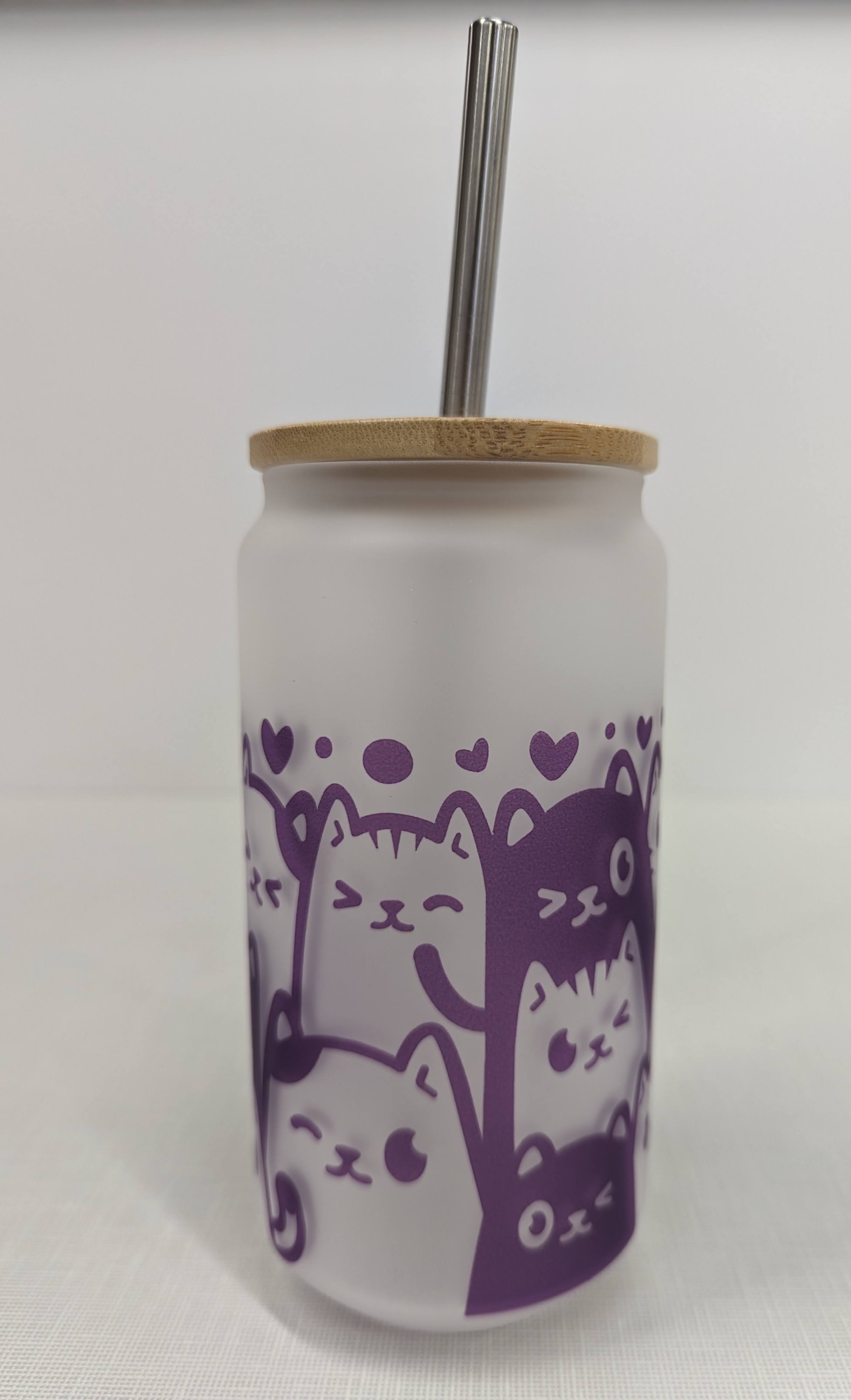 A glass cup with a bamboo top and straw with a purple kitten design around it