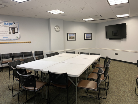 Meeting Room C with tables pushed together to make conference table, chairs at table and placed along wall, and a mounted television