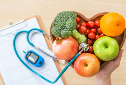 Stethescope with a diabetes testing meter along with a bowl of vegetables in a heart shaped basket.