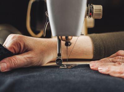 Image shows a two hands guiding dark blue fabric through a sewing machine.