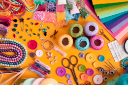 Various craft supplies including scissors, paper, thread and buttons on a yellow background.